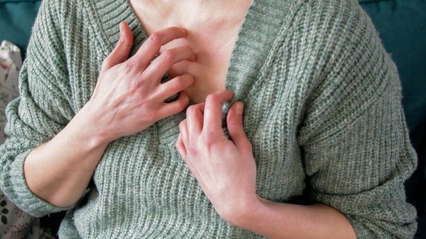 Woman in green knit jumper scratching her chest