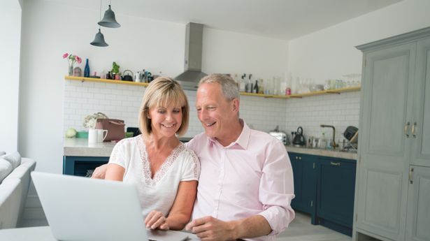 Happy senior couple paying bills online at home from a laptop computer - technology concepts