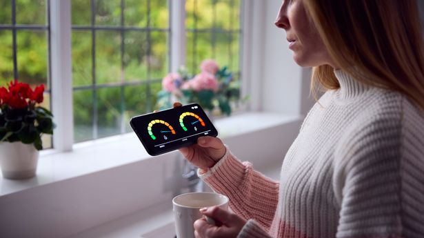 Worried Woman Looking At Smart Meter In Kitchen At Home During Cost Of Living Energy Crisis