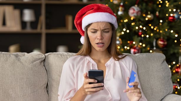 Worried concerned girl in Christmas Santa hat having problems with payment by credit card online for New Year purchases, looking at smartphone screen with puzzled face. Scam, fraud concept