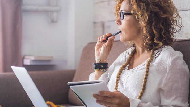 woman thinking and write notes on paper working on a laptop