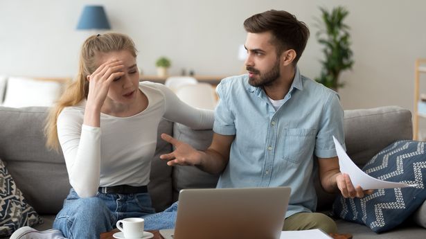 Stressed unhappy couple arguing about huge expenses with laptop and papers, angry husband blaming wife of overspending debt, family having conflict fight about wasting money financial problem at home